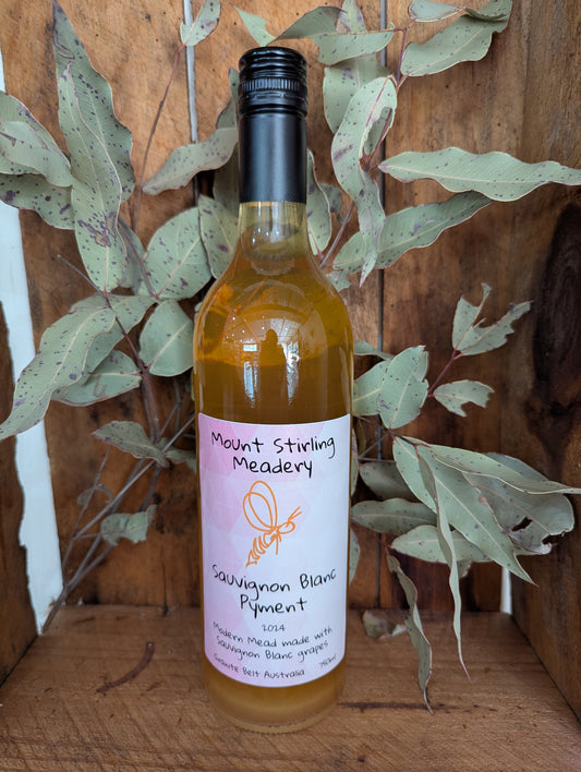 A bottle of Sauvignon Blanc Pyment Mead with a label that includes the brand name and the product name, placed against a wooden background with green foliage.