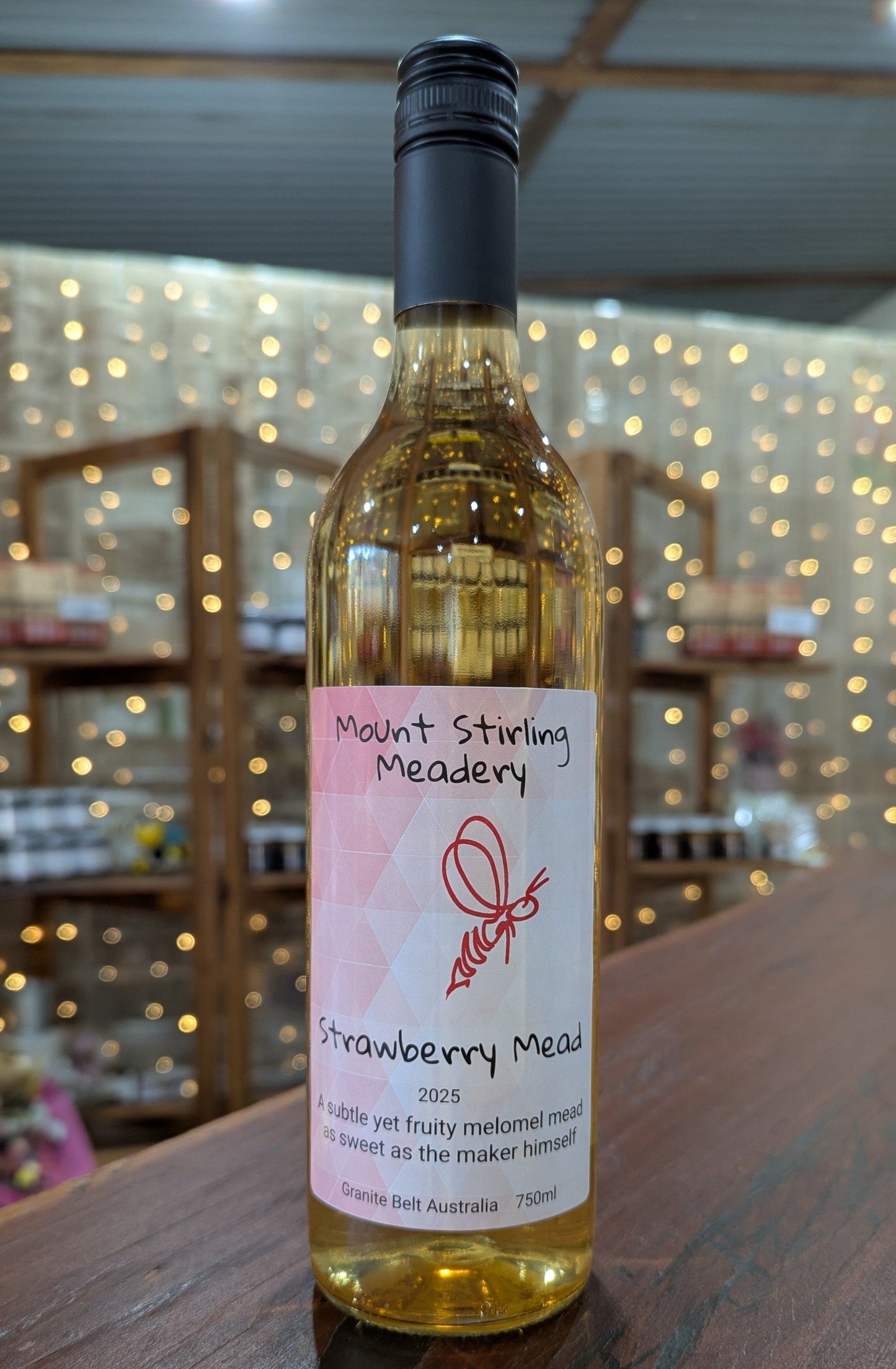 Bottle of Strawberry Mead from Mount Stirling Meadery on a wooden surface with a blurred background.